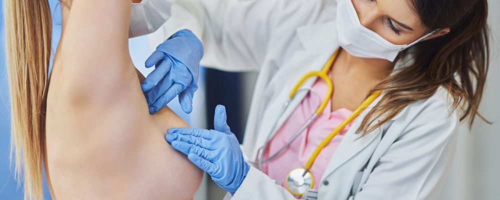 Picture of doctor in mask checking up breast to her patient